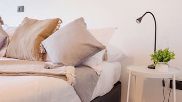 A modern bedroom with a bed, pillows, a bedside table with a lamp, and a framed picture on the wall.