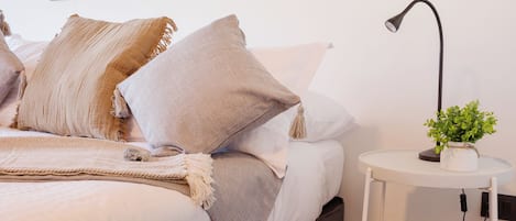 A modern bedroom with a bed, pillows, a bedside table with a lamp, and a framed picture on the wall.