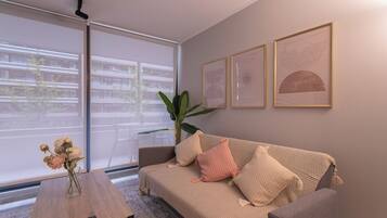 A living room with a sofa, a coffee table, and a plant. There are framed artworks on the wall.
