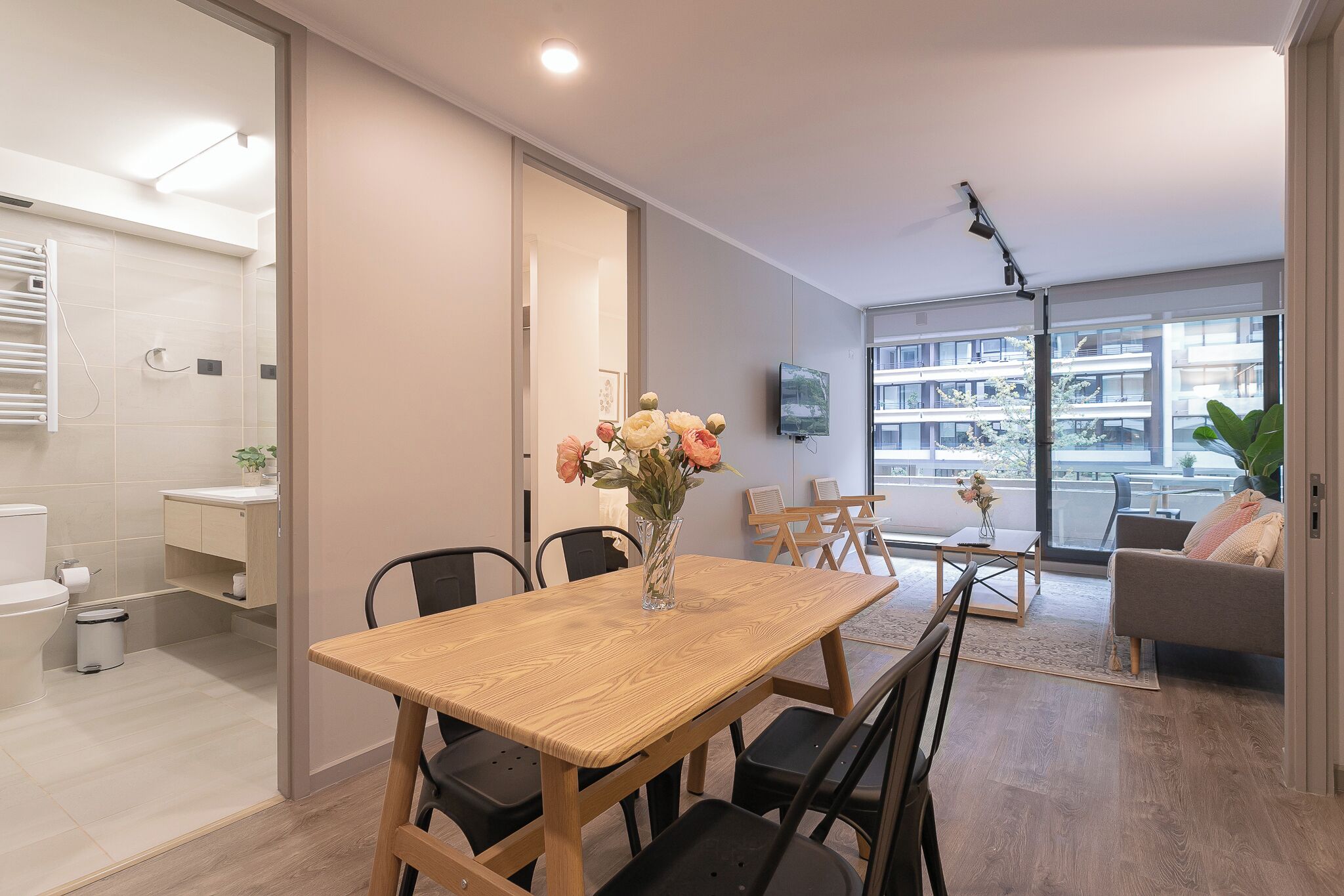 A modern living room with a dining table, chairs, a sofa, and a TV mounted on the wall.