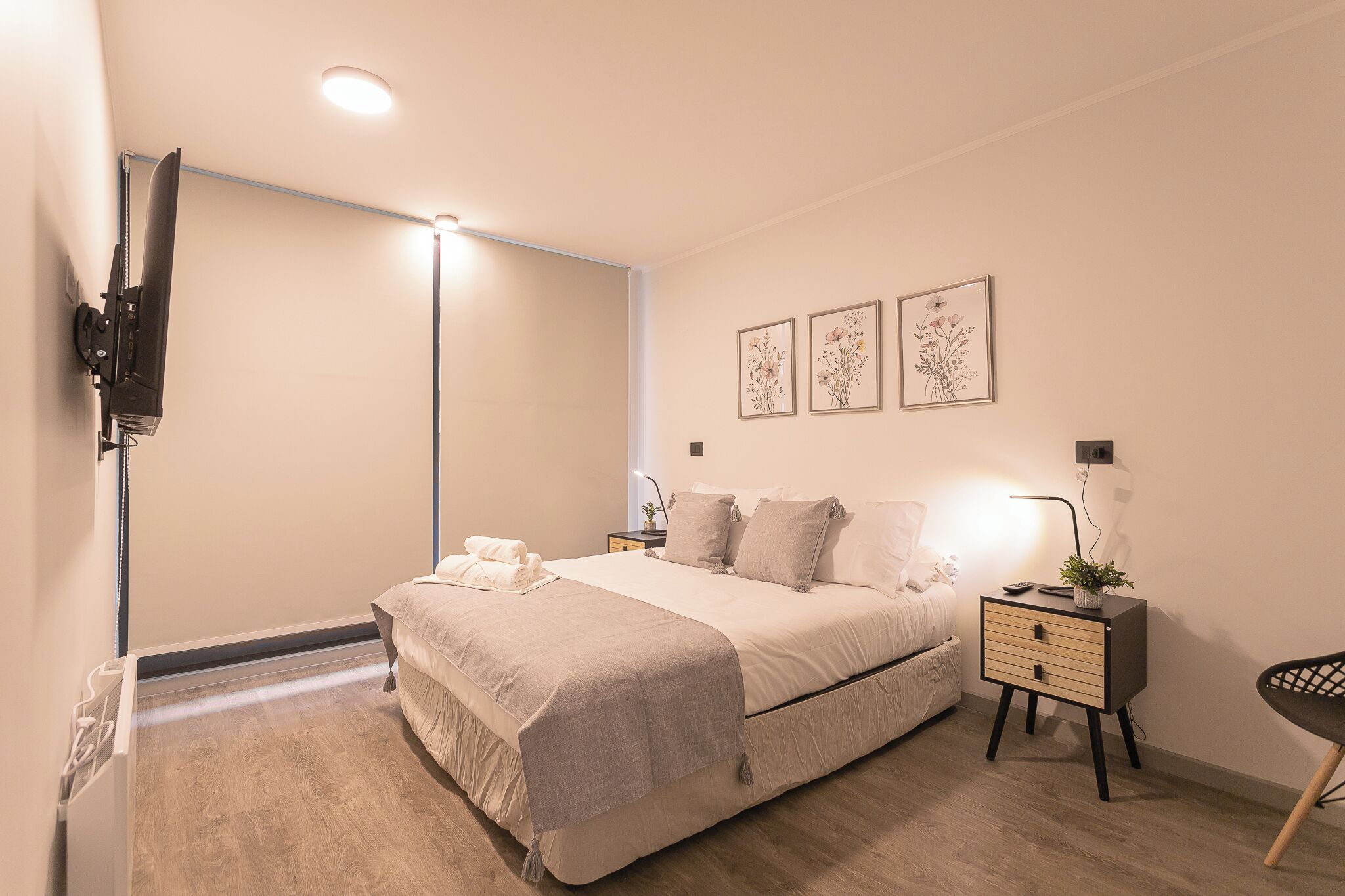 Un dormitorio con cama, mesita de noche, lámpara y una obra de arte en la pared.