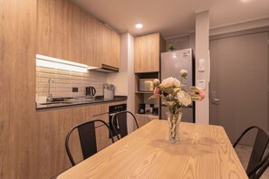 Een moderne keuken met houten kastjes, een eettafel, stoelen, een koffieapparaat en een koelkast.