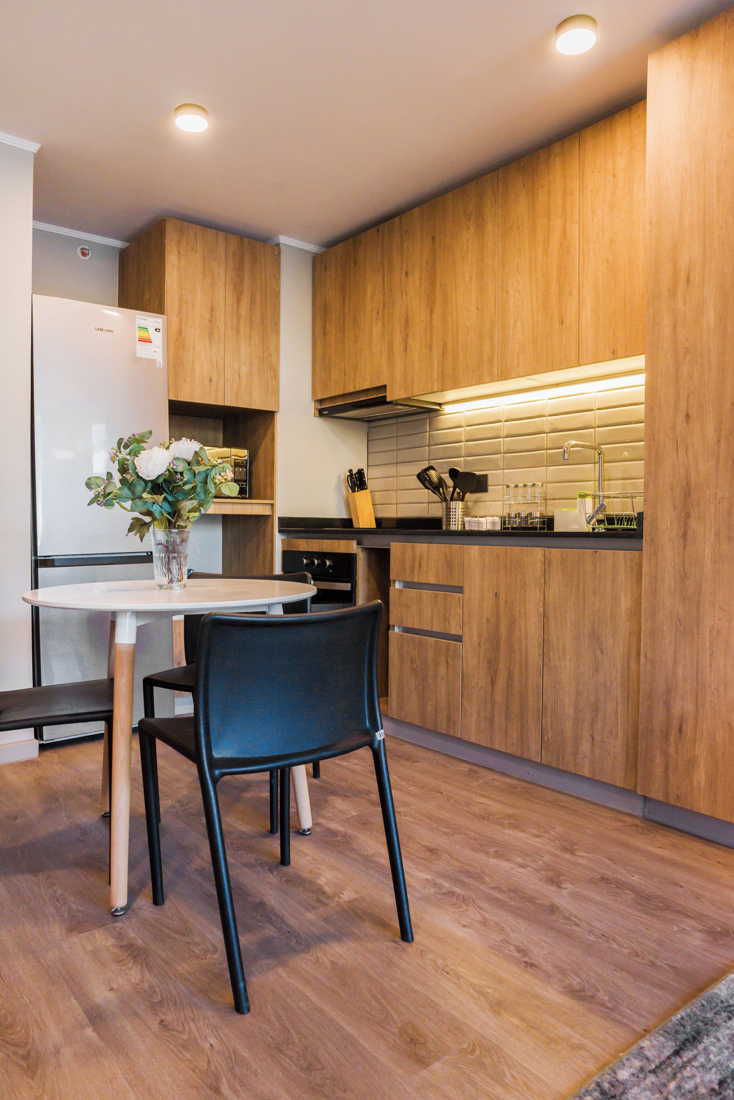 A modern kitchen with wooden cabinets, a white refrigerator, and a dining area with a table and chairs.
