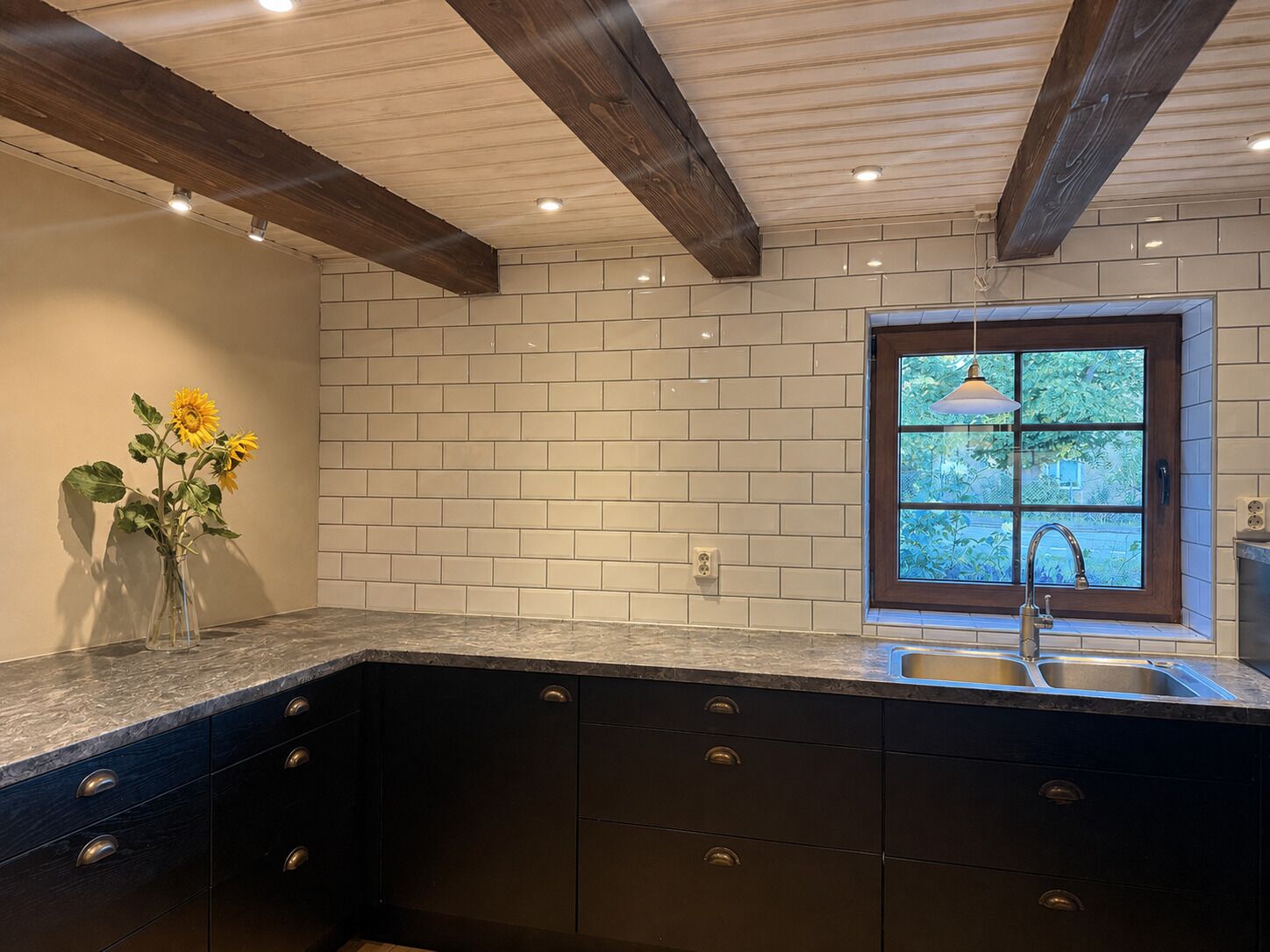A kitchen with a dark countertop, white subway tiles, and a window with a view of greenery.
