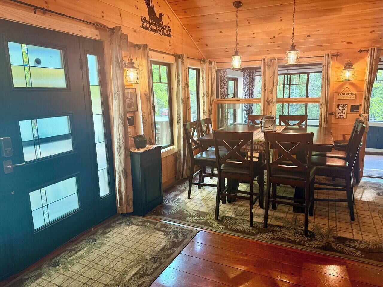 A wooden interior with a dining area featuring a table and chairs, a black door with windows, and a sign on the wall.