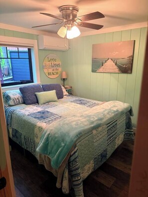 Ein Schlafzimmer mit Bett, Deckenventilator, Fenster und einem Bild an der Wand.