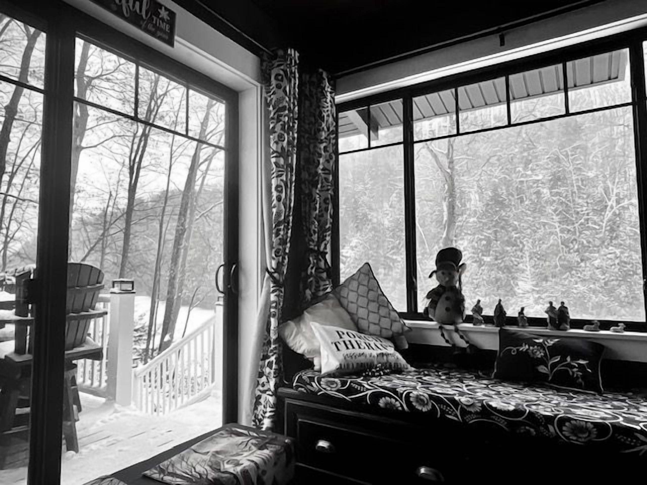 A room with a large window, a bed with patterned bedding, and a view of trees outside.