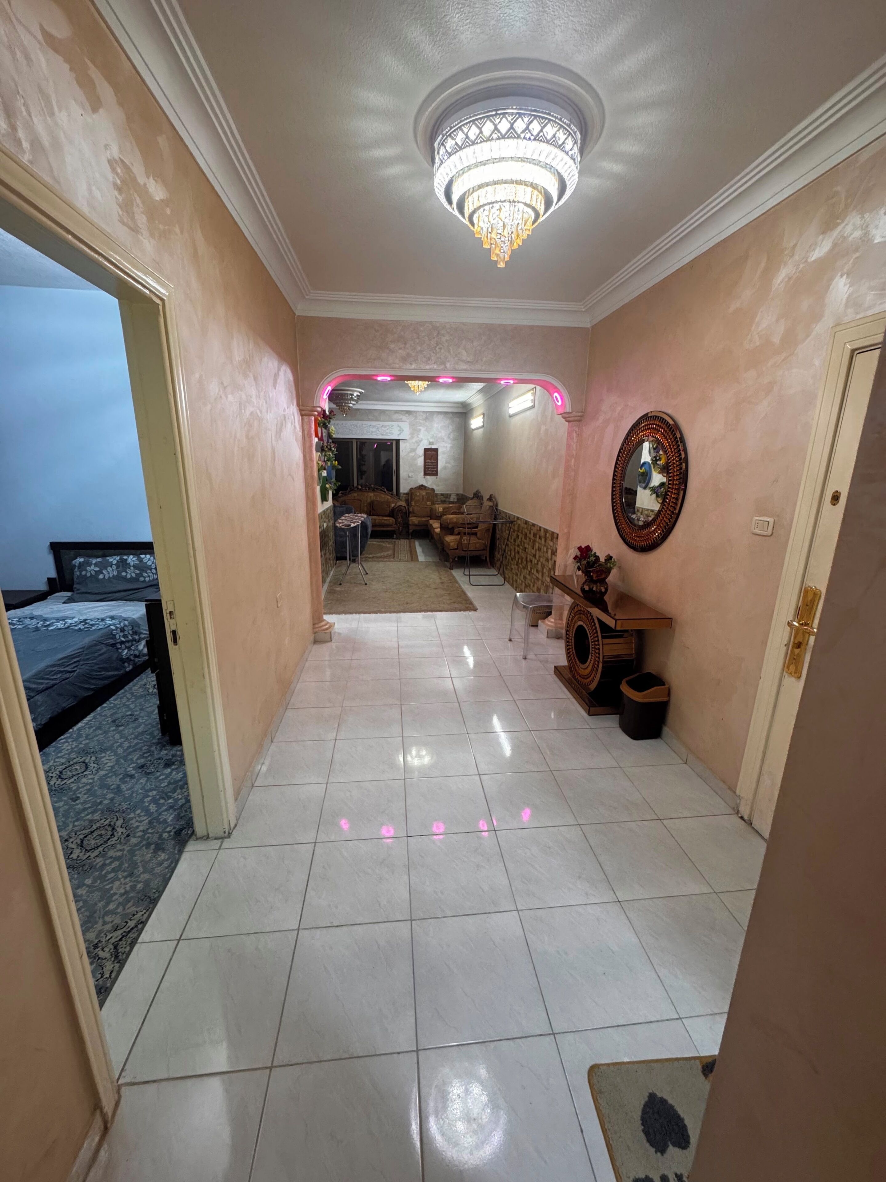 A hallway with a chandelier, a sofa set, and a mirror on the wall.