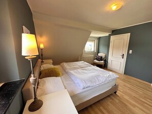 A bedroom with a bed, bedside lamps, a chair, a window, and a door. - Unter dem Ginster - 12-Person Villa Next to the Forest - Brilon Wald - Sauerland Willingen (Brilon)