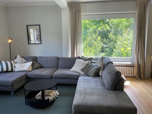 A modern living room with a sectional sofa, a round coffee table, and a large window with curtains. - Unter dem Ginster - 12-Person Villa Next to the Forest - Brilon Wald - Sauerland Willingen (Brilon)