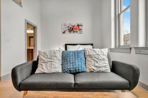 Ein modernes Wohnzimmer mit grauem Sofa, einem Bild an der Wand und einem Fenster, das natürliches Licht hereinlässt.