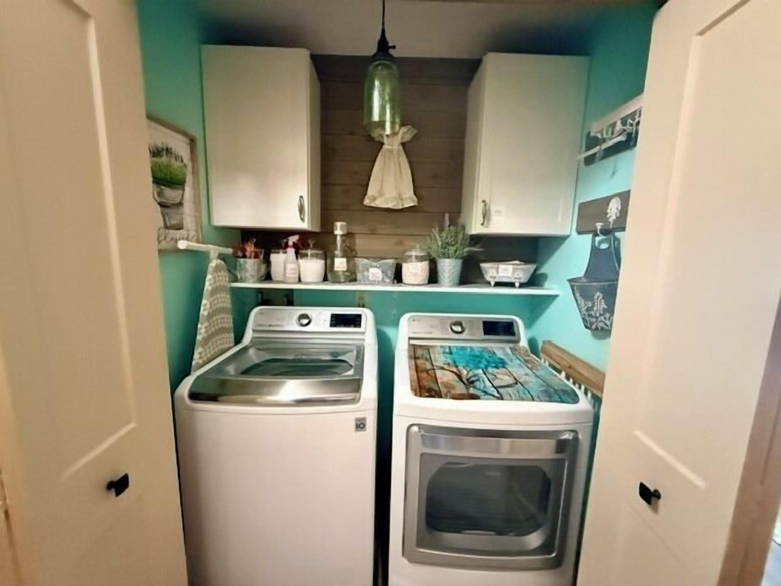 A compact laundry room with two washing machines, a dryer, and a hanging light fixture.