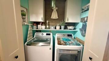 A compact laundry room with two washing machines, a dryer, and a hanging light fixture.