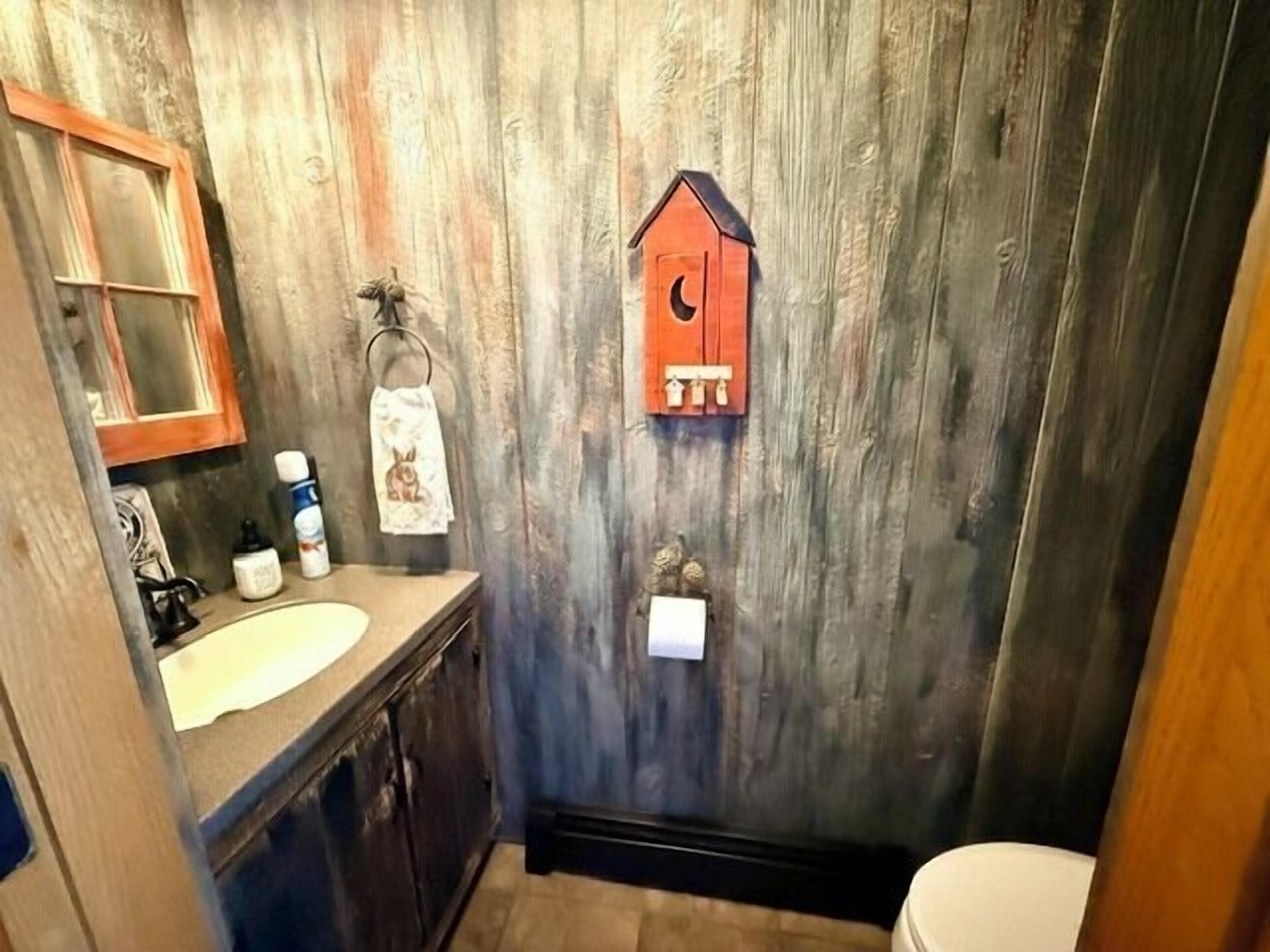Ein rustikales Badezimmer mit Holzwand, einem Waschbecken, einer Toilette und einem hängenden Handtuchhalter.