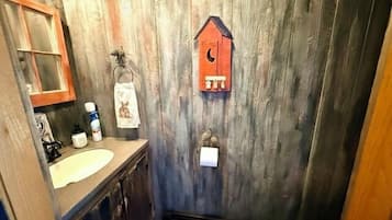 Ein rustikales Badezimmer mit Holzwand, einem Waschbecken, einer Toilette und einem hängenden Handtuchhalter.