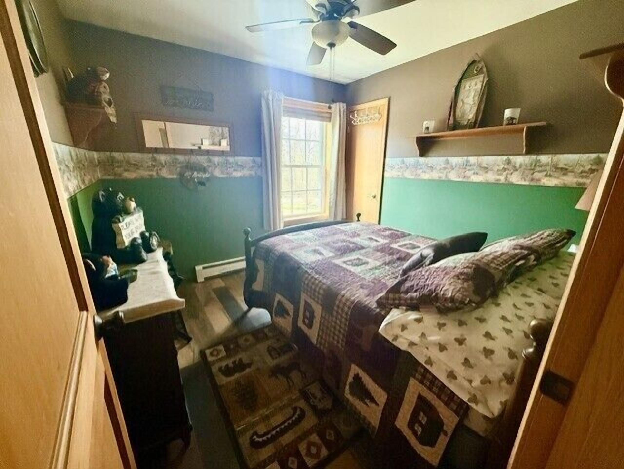 Une chambre à coucher avec un lit, une commode, une fenêtre et un ventilateur de plafond.