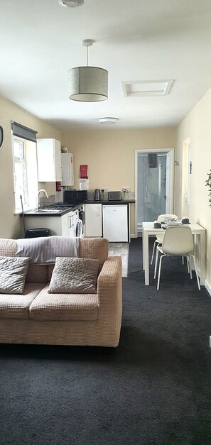 A compact living space with a sofa, a dining table, and a kitchenette. - Clacton 1 Bed Flat | Near Beach, Town & Station (Essex)