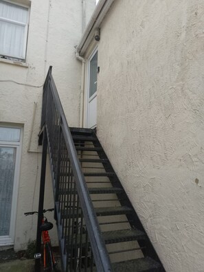 A narrow stairway leading to a door, with a bicycle parked against the wall. - Clacton 1 Bed Flat | Near Beach, Town & Station (Essex)