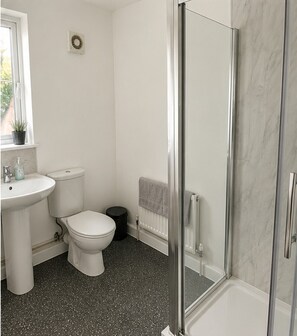 A bathroom with a white toilet, sink, and shower area. - Clacton 1 Bed Flat | Near Beach, Town & Station (Essex)