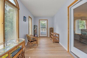 A hallway with a glass door leading to a balcony, wicker furniture, and a bookshelf. - SH30: Southern Shores 30 (Southern Shores)