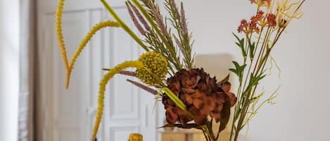 Une table à manger avec une bouteille de champagne, une bougie, un panier de fruits et un vase rempli de fleurs.