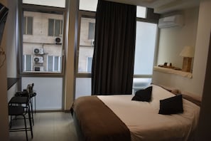 Ein Hotelzimmer mit Bett, Schreibtisch mit Stuhl, einem Fenster mit Vorhängen und einer Klimaanlage an der Wand.