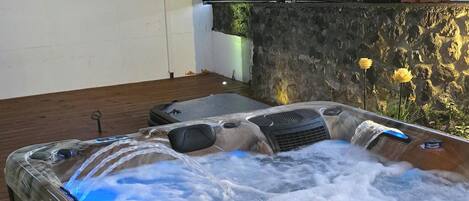 A hot tub with a wooden deck and a stone wall in the background.
