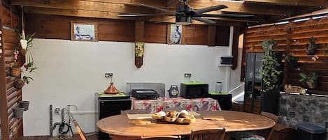 A rustic outdoor kitchen with a wooden table, hanging lights, and a ceiling fan.