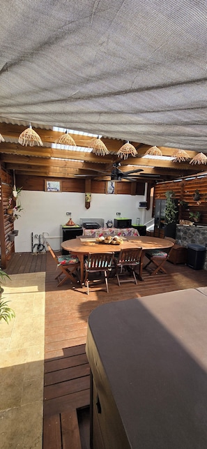 A rustic outdoor kitchen with a wooden table, hanging lights, and a ceiling fan. - Stunning Master Suite with Spa and Breakfast Included (Saint-Pierre)