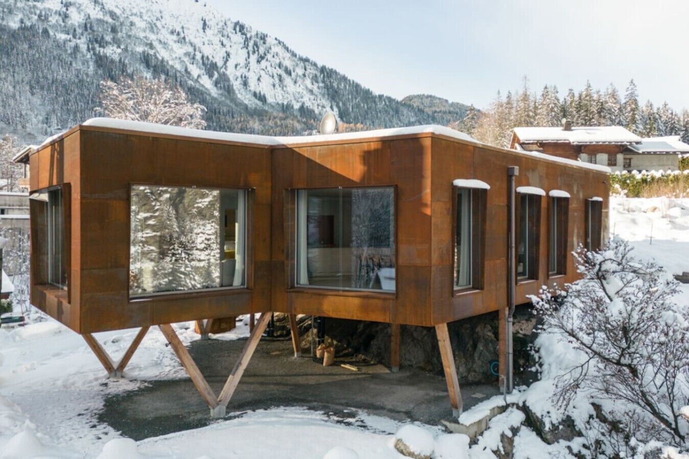 A modern wooden cabin with large windows, set in a snowy mountainous area.