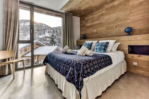 A bedroom with a large window, a bed with a patterned blanket, and wooden paneling on the walls. - Skyfall - Modern Chalet | Sleeps 10 | Unique Design | View (Les Houches)