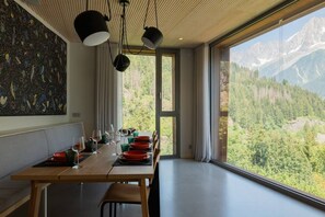 A dining area with a table set for four, large windows offering a mountain view, and pendant lighting. - Skyfall - Modern Chalet | Sleeps 10 | Unique Design | View (Les Houches)