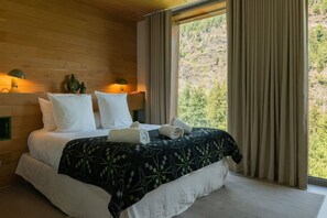 A bed with white linens and a patterned blanket, two pillows, and two rolled towels on a wooden floor. - Skyfall - Modern Chalet | Sleeps 10 | Unique Design | View (Les Houches)