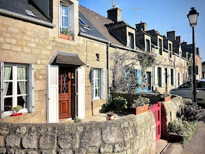 A row of stone houses with traditional architecture, featuring wooden doors and shutters, and a stone wall in the foreground. - MAISON BARFLEUR Historic cottage by the sea between the harbor and the beach. (Barfleur)