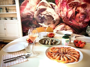A dining table set with plates, glasses, and cutlery, with a floral painting in the background. - MAISON BARFLEUR Historic cottage by the sea between the harbor and the beach. (Barfleur)