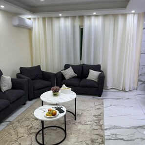 A modern living room with a sectional sofa, a marble coffee table, and a potted plant. - 3-bedroom apartment in enjoyable Amman with AC for relaxing stay (Amman)