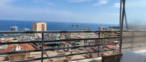 A balcony with a view of a coastal cityscape, including buildings and the sea.