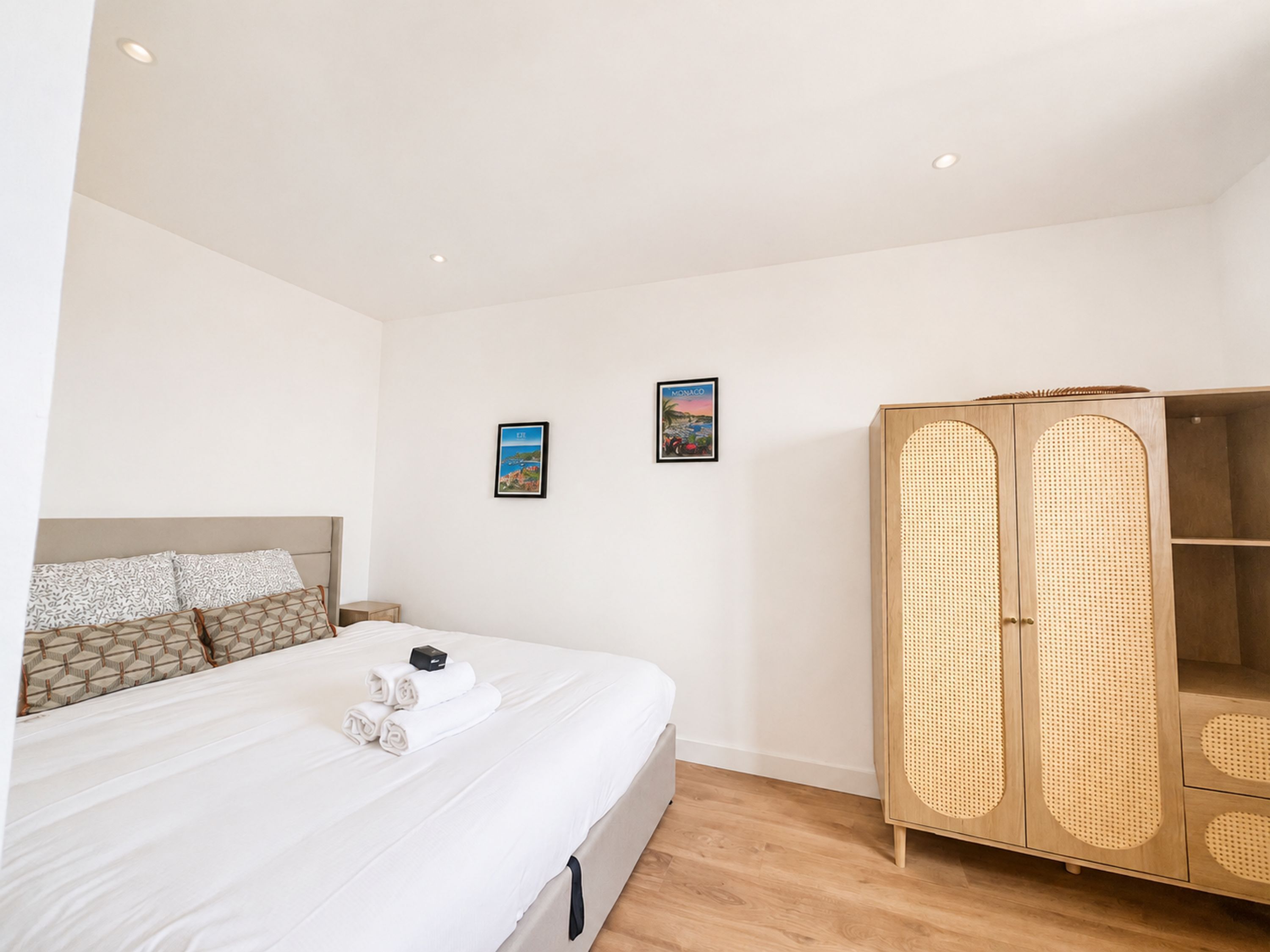 Quarto de hotel com uma cama, duas imagens emolduradas na parede e um guarda-roupa de madeira.