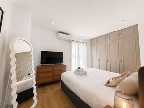 Ein Hotelzimmer mit einem Bett, einem Fernseher auf einer Holzkommode, einem Spiegel und einem Fenster mit Vorhängen.
