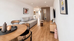 Ein modernes Wohnzimmer mit einer Couch, einem Esstisch mit Stühlen, einem Fernseher und Kunstwerken an den Wänden.