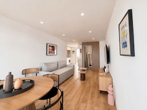 A modern living room with a sofa, a dining table with chairs, a TV, and artwork on the walls. - 2BR Sea View Central 1 Min From Monaco (Beausoleil)