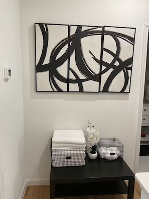 A room with a black abstract painting, a black table with a white vase and white flowers, and a white towel on the table. - Rezidence Townhome at Dignowity (San Antonio)