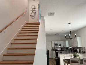 A staircase leading to a kitchen with white cabinets, a microwave, and a chandelier. - Rezidence Townhome at Dignowity (San Antonio)