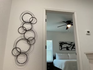 A room with a white wall, a ceiling fan, a bed with white bedding, and a door leading to another room. - Rezidence Townhome at Dignowity (San Antonio)