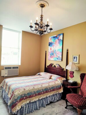 Une chambre à coucher avec un lit, un lustre, un tableau, un climatiseur et une chaise.