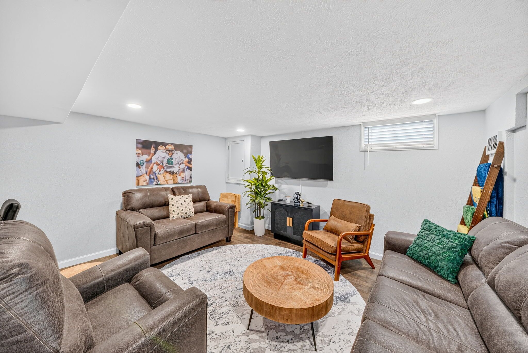 A modern living room with leather sofas, a round wooden coffee table, and a flat-screen TV mounted on the wall.