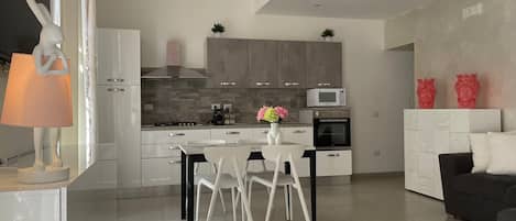 Een moderne keuken met een eethoek, witte kasten en een grijze bank.
