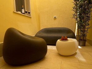 Ein modernes Interieur mit zwei schwarzen Sofas, einem weißen Hocker und einer Zimmerpflanze.