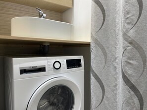 Eine Waschmaschine mit Bedienfeld, ein Waschbecken darüber und einer Wand mit Muster.