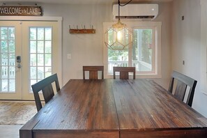 A dining room with a large wooden table, chairs, a hanging light fixture, and a 'Welcome to the Lake' sign.